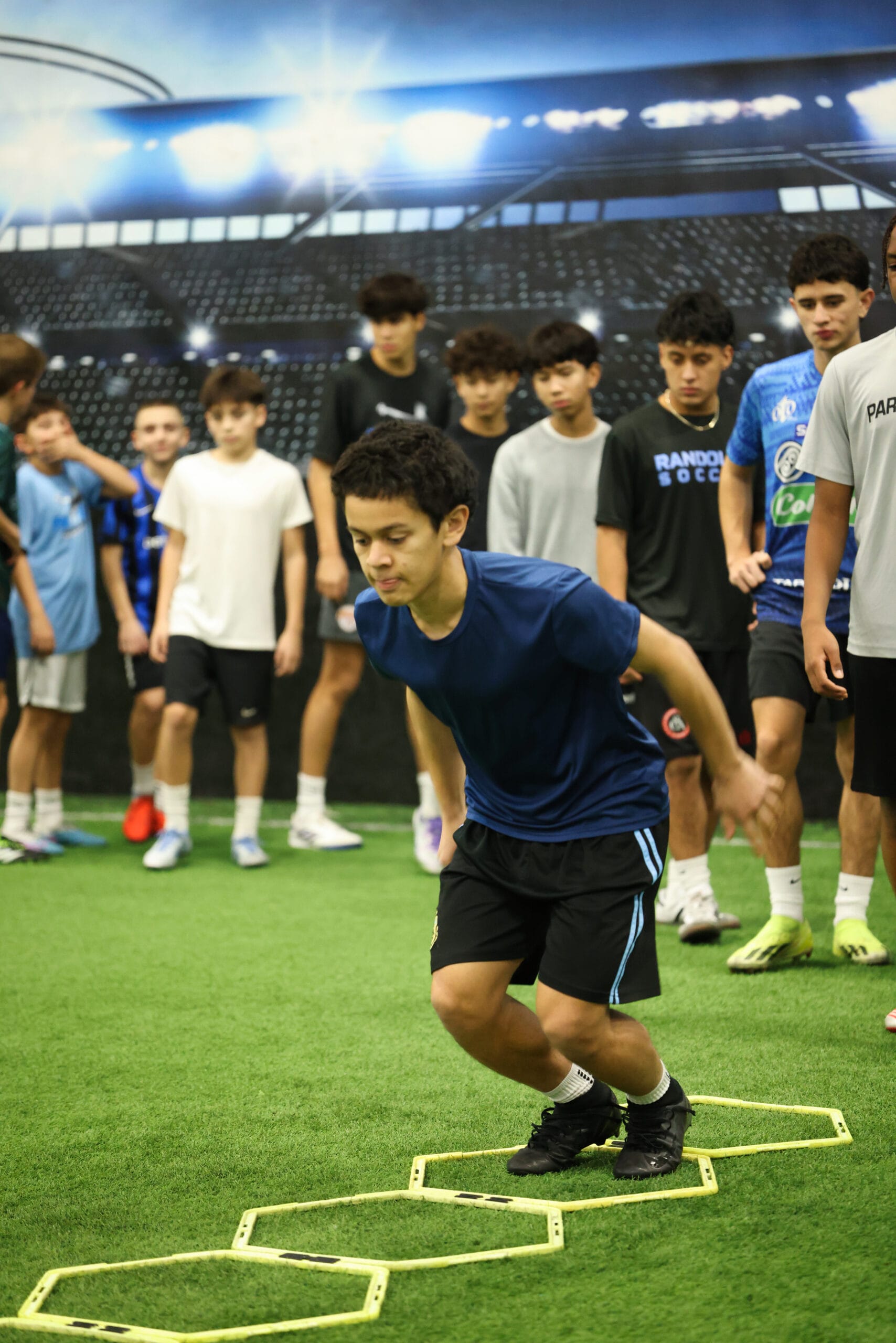5K2A0368 Youth soccer player performing agility ladder drill during indoor training session at Pro Soccer Academy while teammates observe