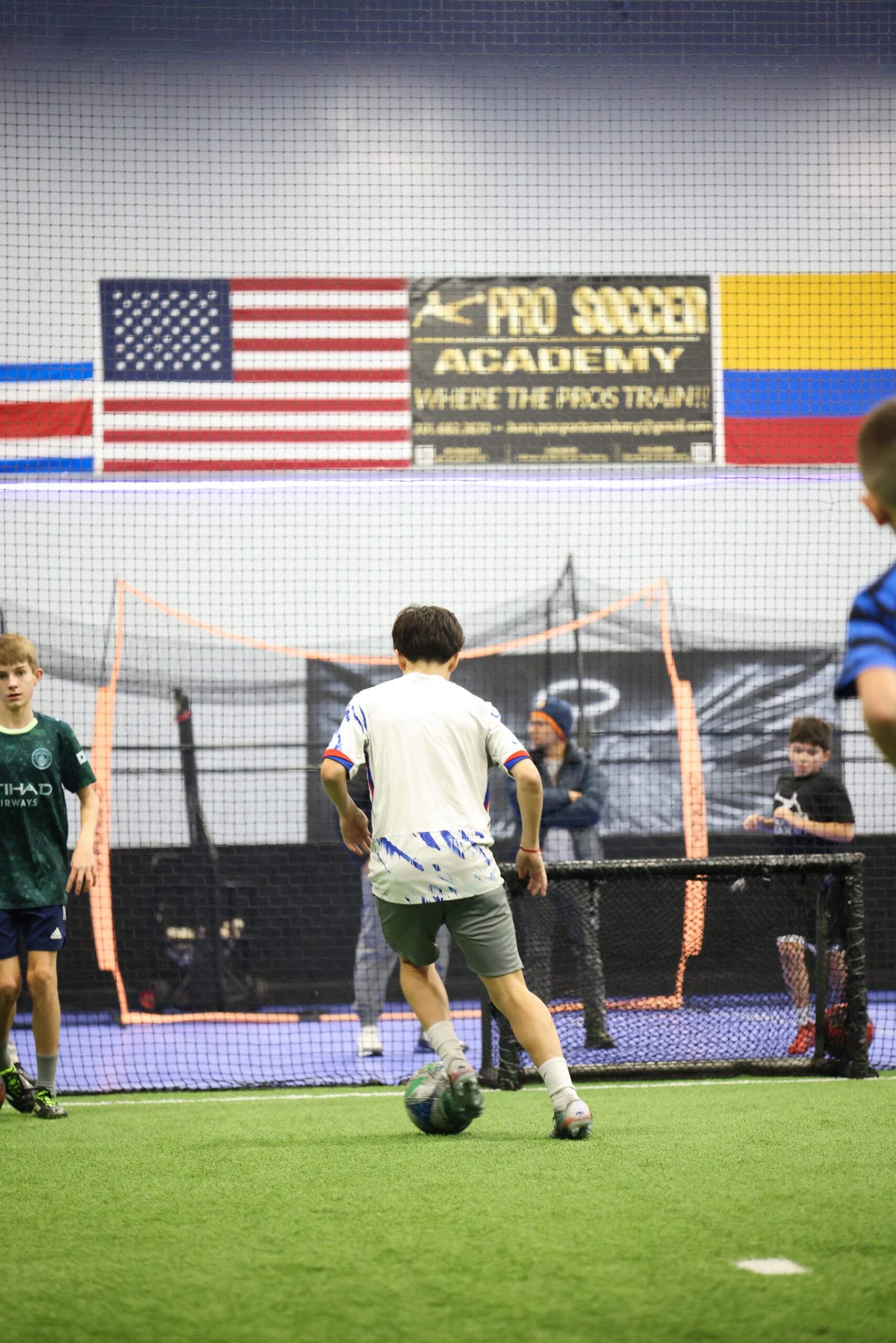 5K2A0393 Youth soccer player dribbling toward goal during indoor training session at Pro Soccer Academy while teammates observe