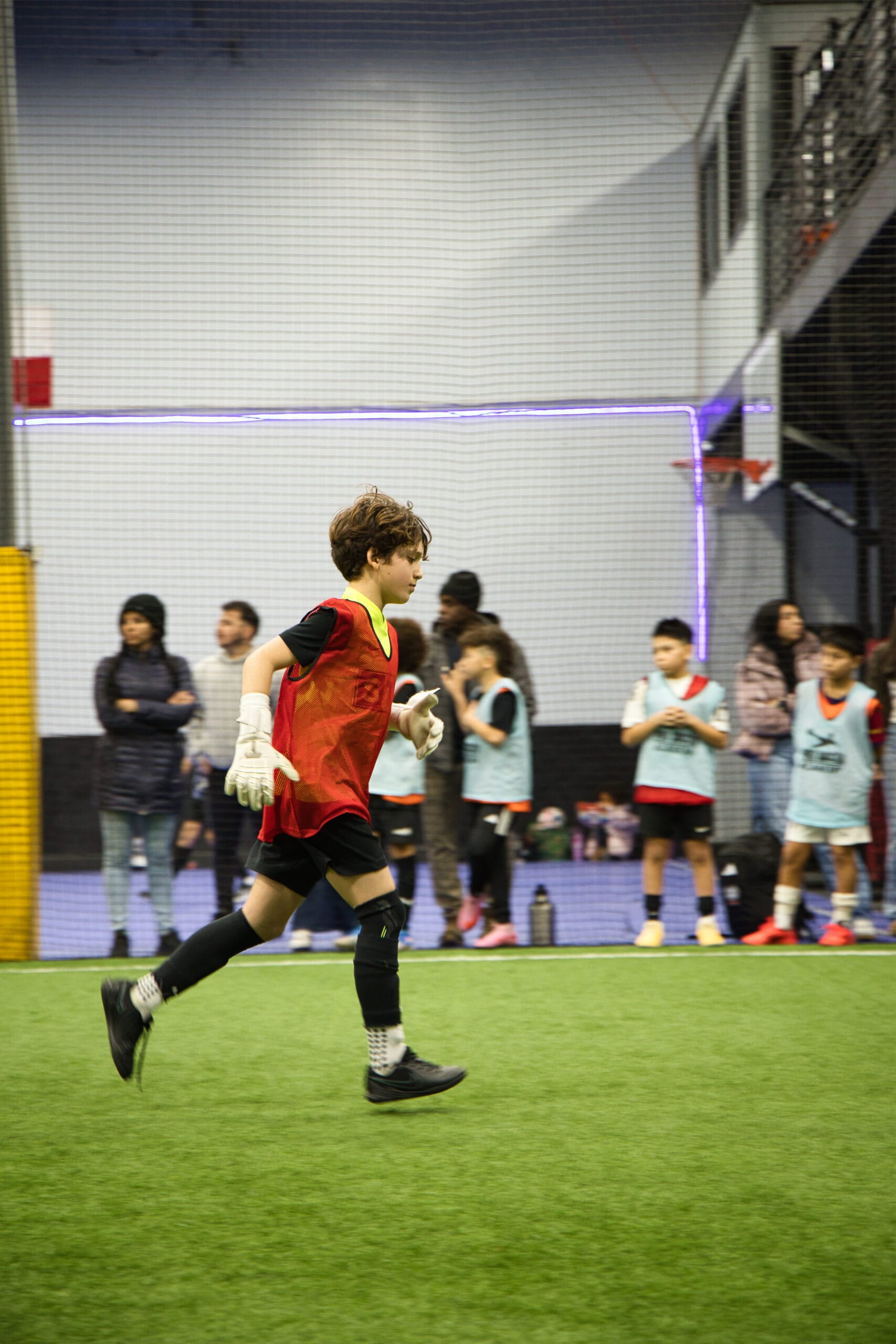 4Q8A0158 Youth goalkeeper in red training bib running across indoor turf during Pro Soccer Academy tryouts