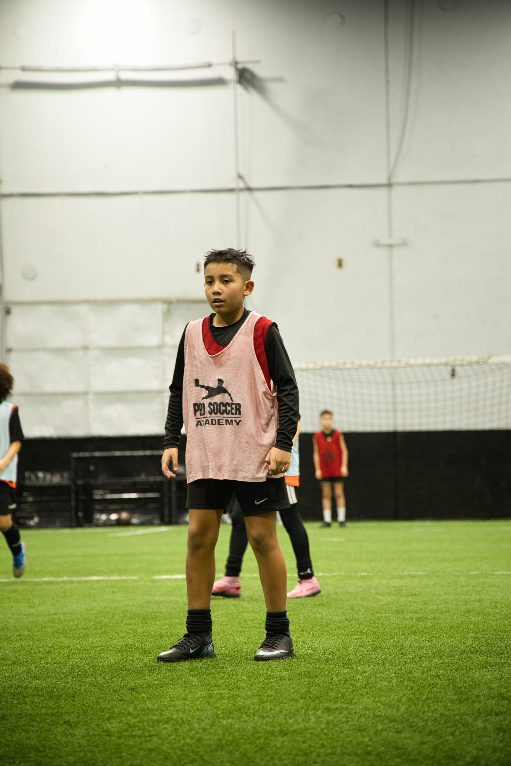 4Q8A0174 Young player in pink Pro Soccer Academy training bib standing ready on indoor turf field