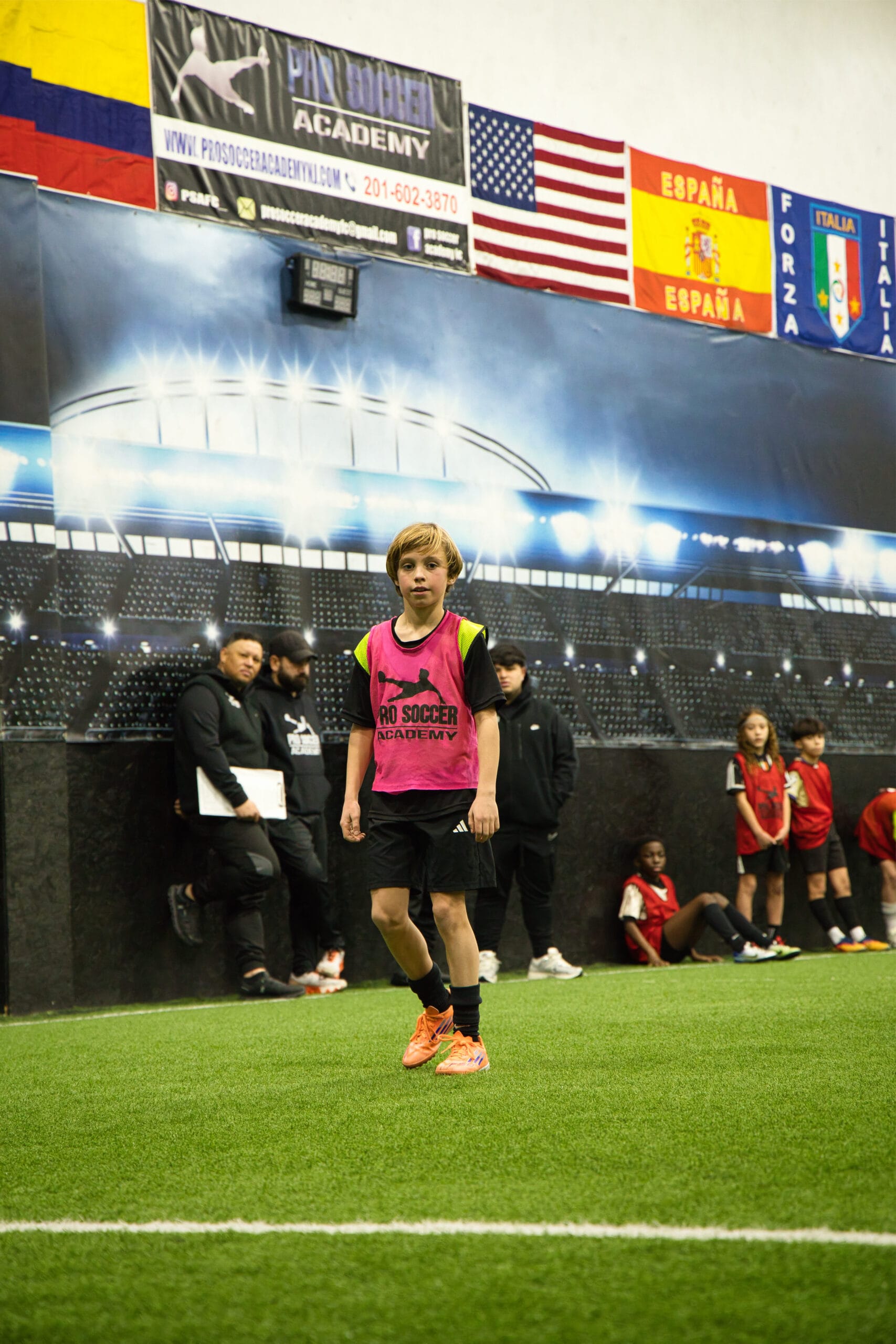 4Q8A0183 Pro Soccer Academy player in pink bib walking on indoor turf with coaches observing in background