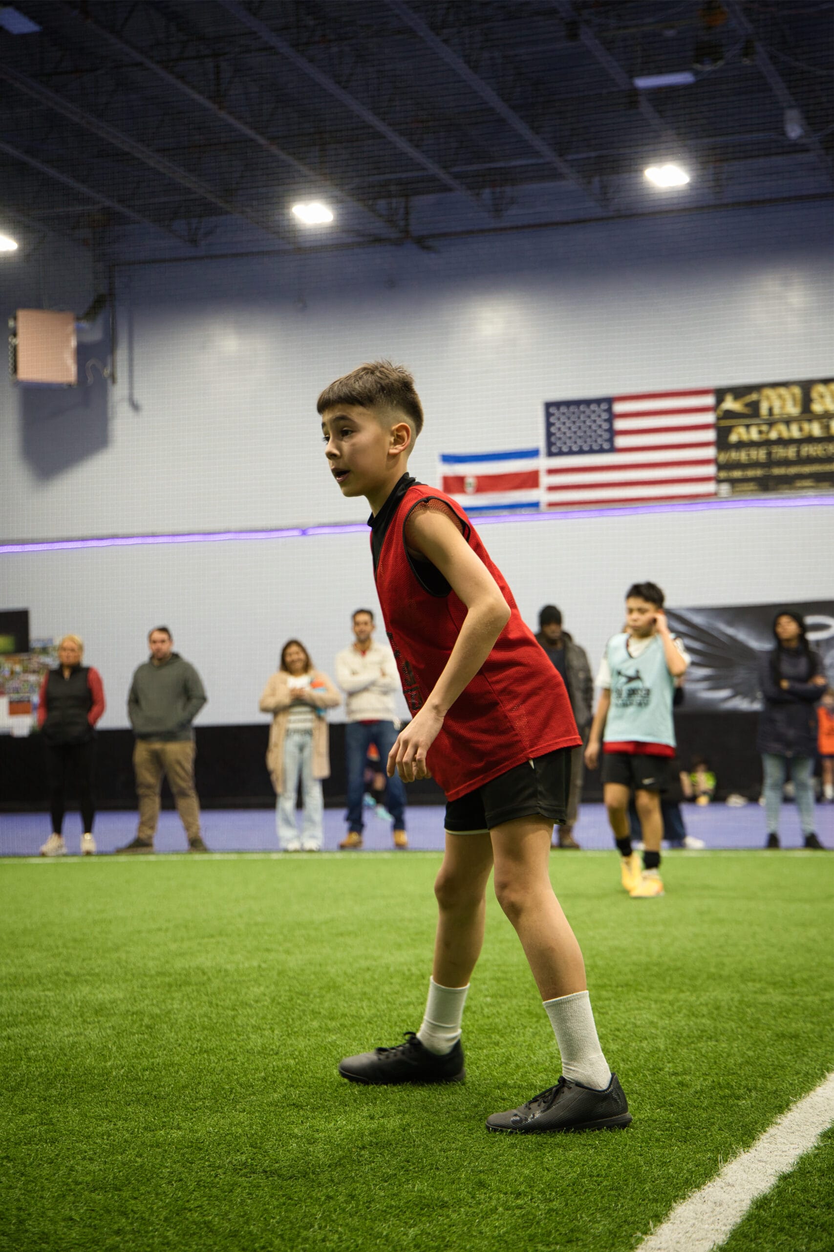 4Q8A0218 Pro Soccer Academy player in light blue bib walking toward camera on indoor turf field