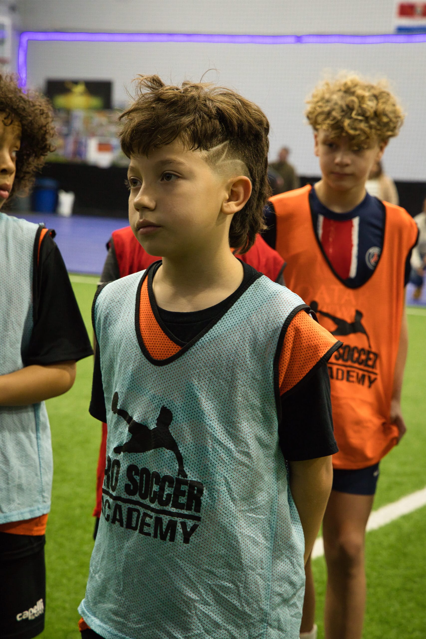 4Q8A0243 Young soccer player wearing blue Pro Soccer Academy training pinnie standing focused during indoor tryouts