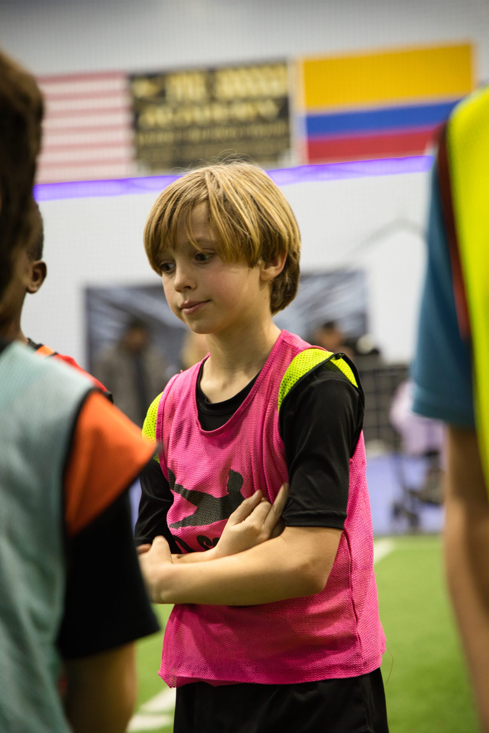 4Q8A0247 Young athlete wearing pink training pinnie at Pro Soccer Academy indoor soccer tryouts, arms crossed and focused.