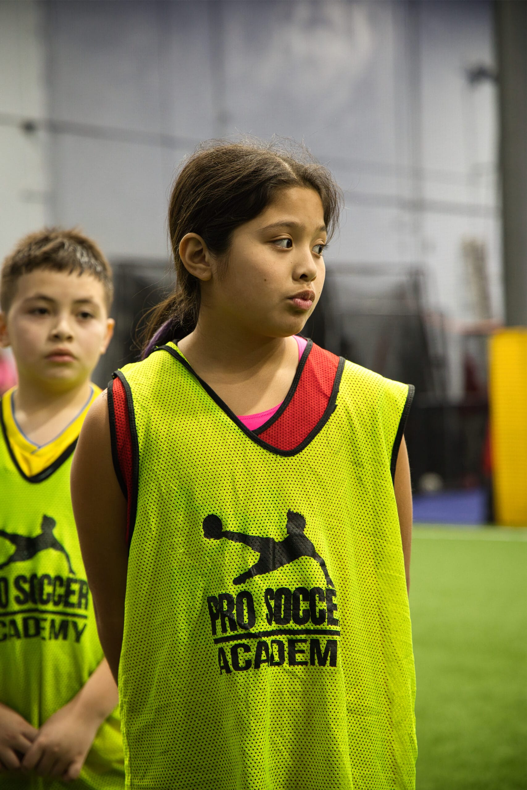 4Q8A0248 Youth soccer player in neon yellow Pro Soccer Academy pinnie standing on indoor turf during competitive tryout session.
