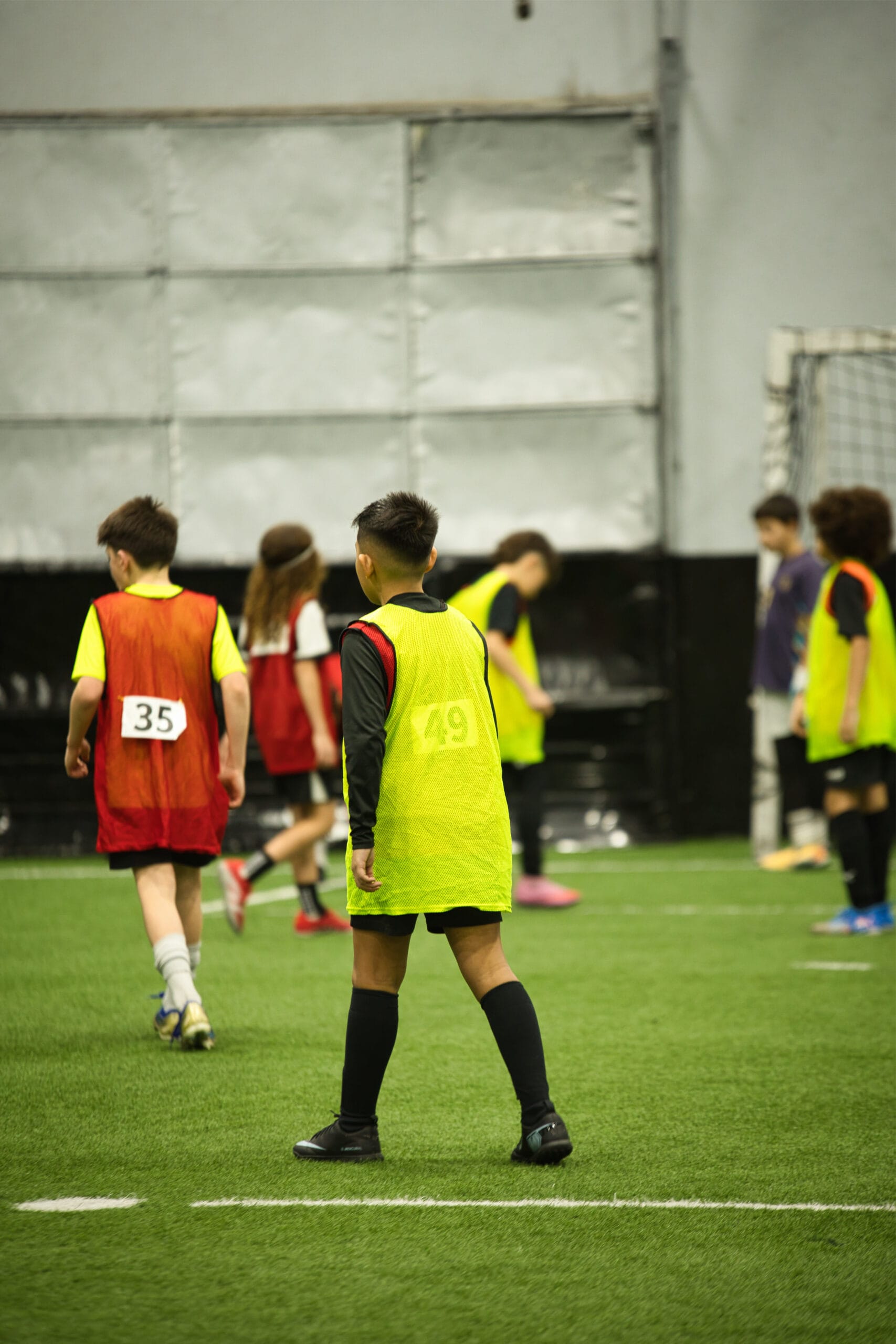 4Q8A0260 Young soccer player in yellow pinnie number 49 walking into position during indoor academy scrimmage.