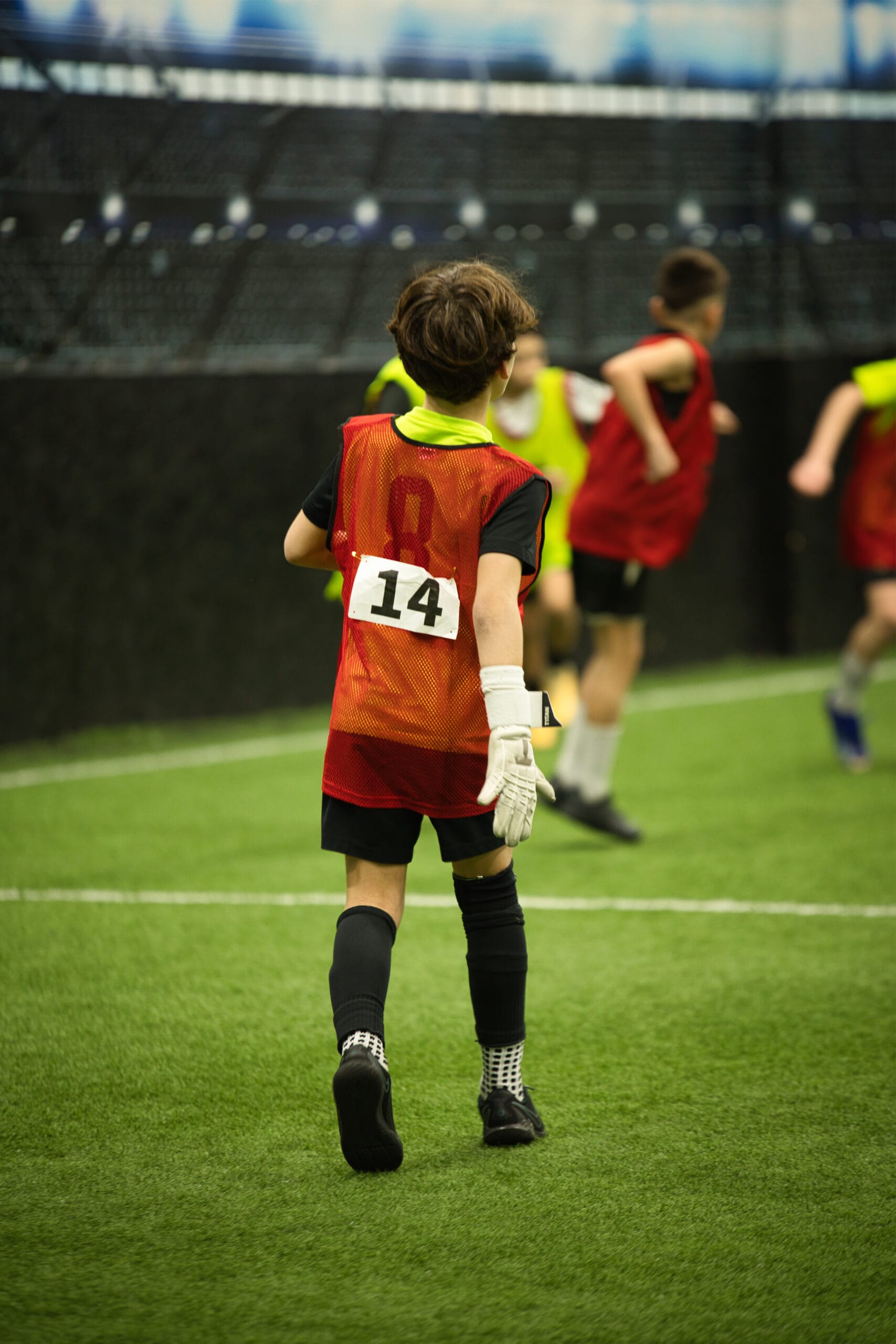 4Q8A0264 Young soccer player wearing red number 14 pinnie running up indoor turf during competitive youth scrimmage.