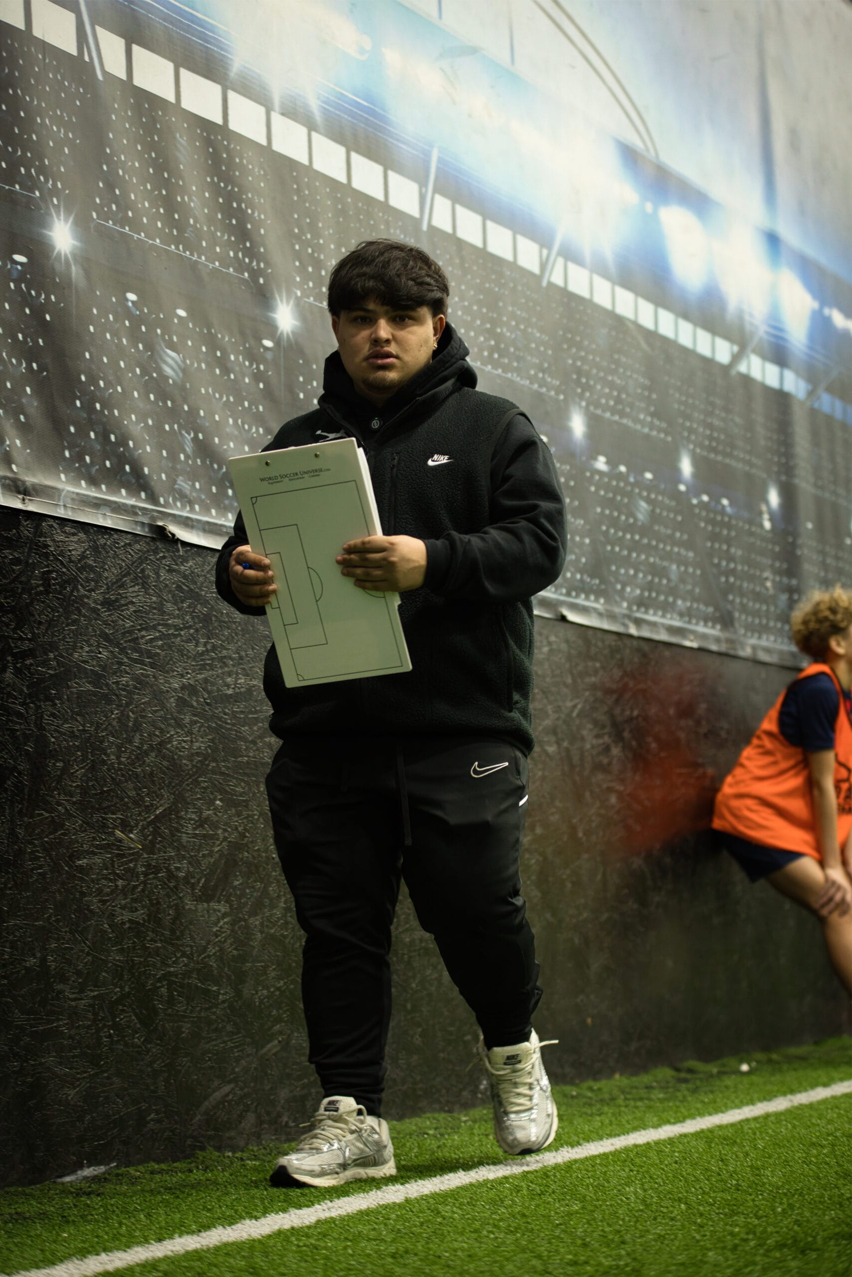 4Q8A0284 Pro Soccer Academy coach holding tactical clipboard on indoor turf during youth soccer evaluation session.