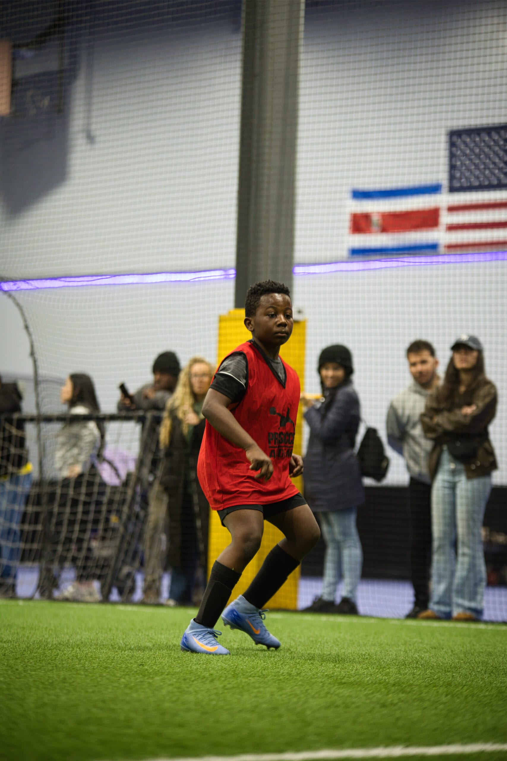 4Q8A0298 Young soccer player in red Pro Soccer Academy pinnie positioning defensively on indoor turf during scrimmage.