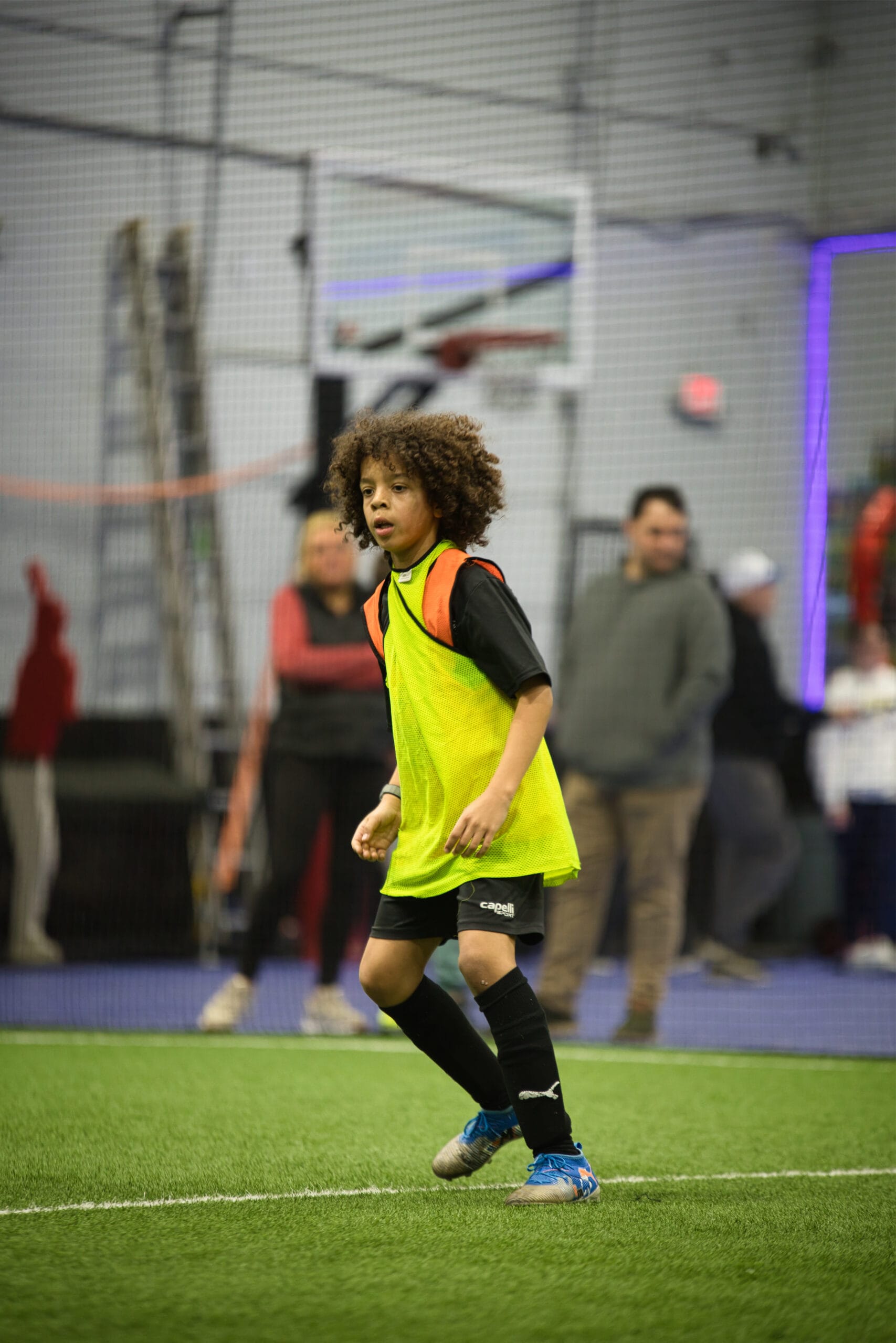 4Q8A0313 Youth soccer player with curly hair in neon yellow pinnie moving into position during indoor Pro Soccer Academy scrimmage.