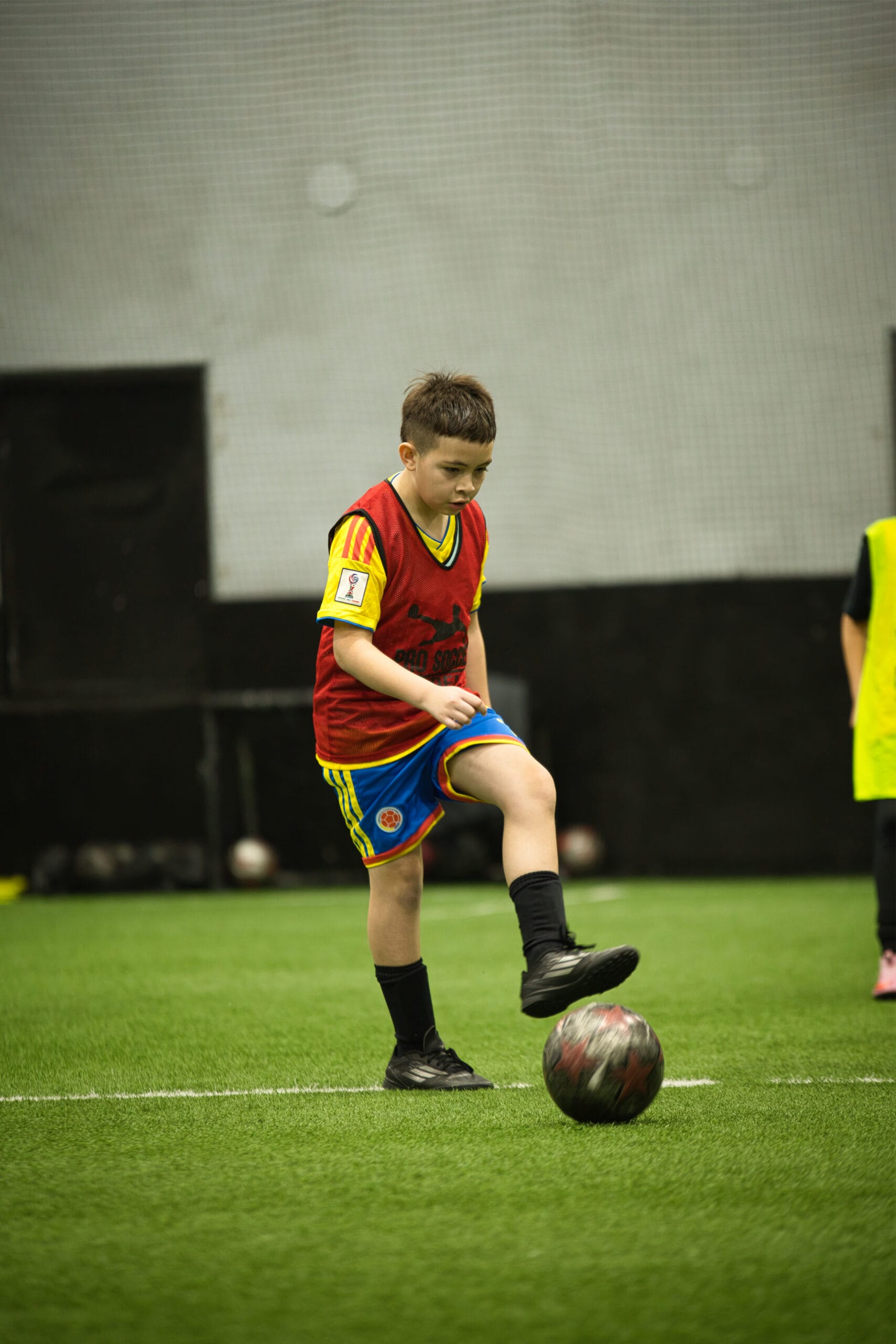 4Q8A0324 Young soccer player in red pinnie stopping the ball with foot during indoor academy scrimmage.
