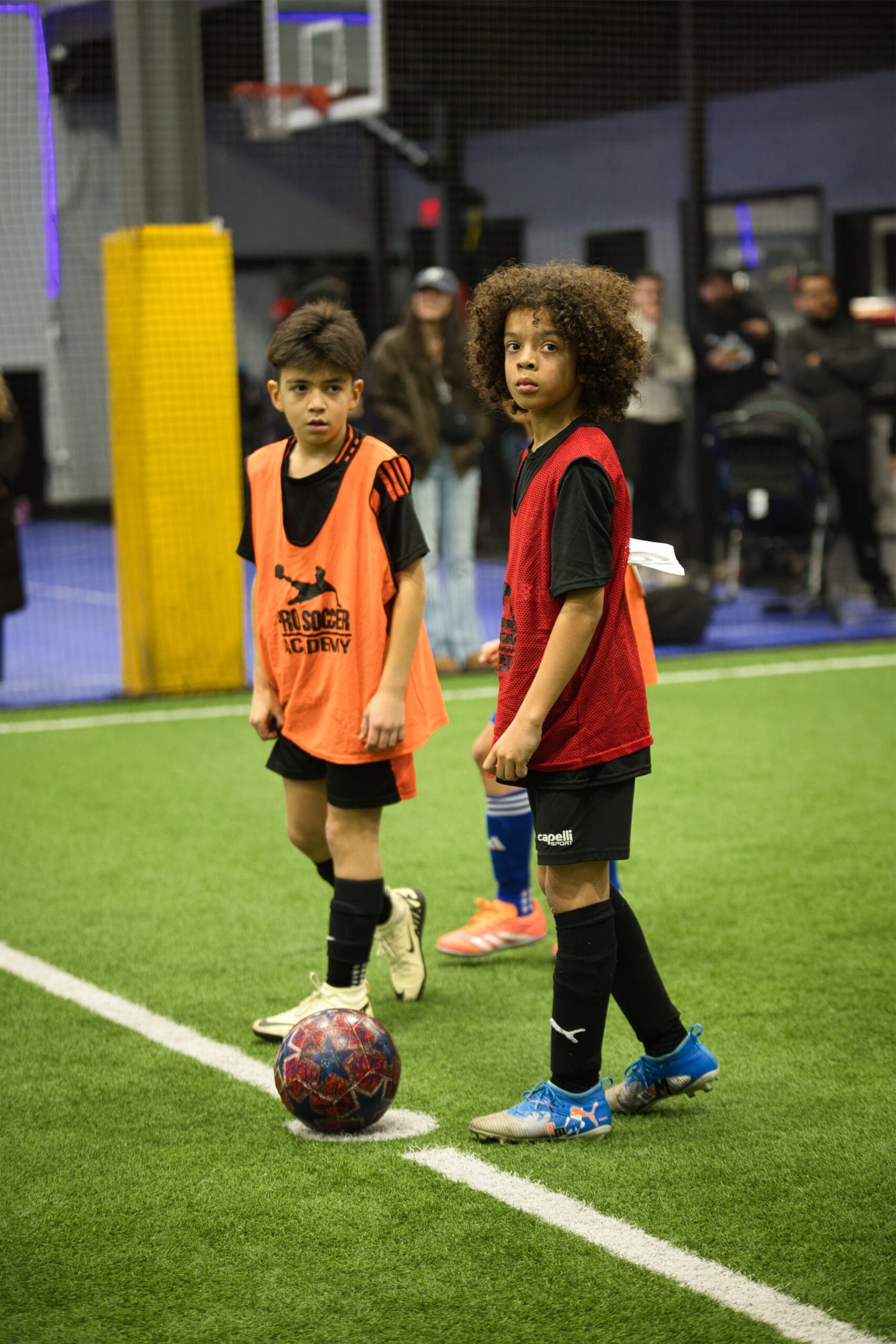 4Q8A0343 Two youth soccer players waiting for restart with ball at sideline during Pro Soccer Academy indoor match.