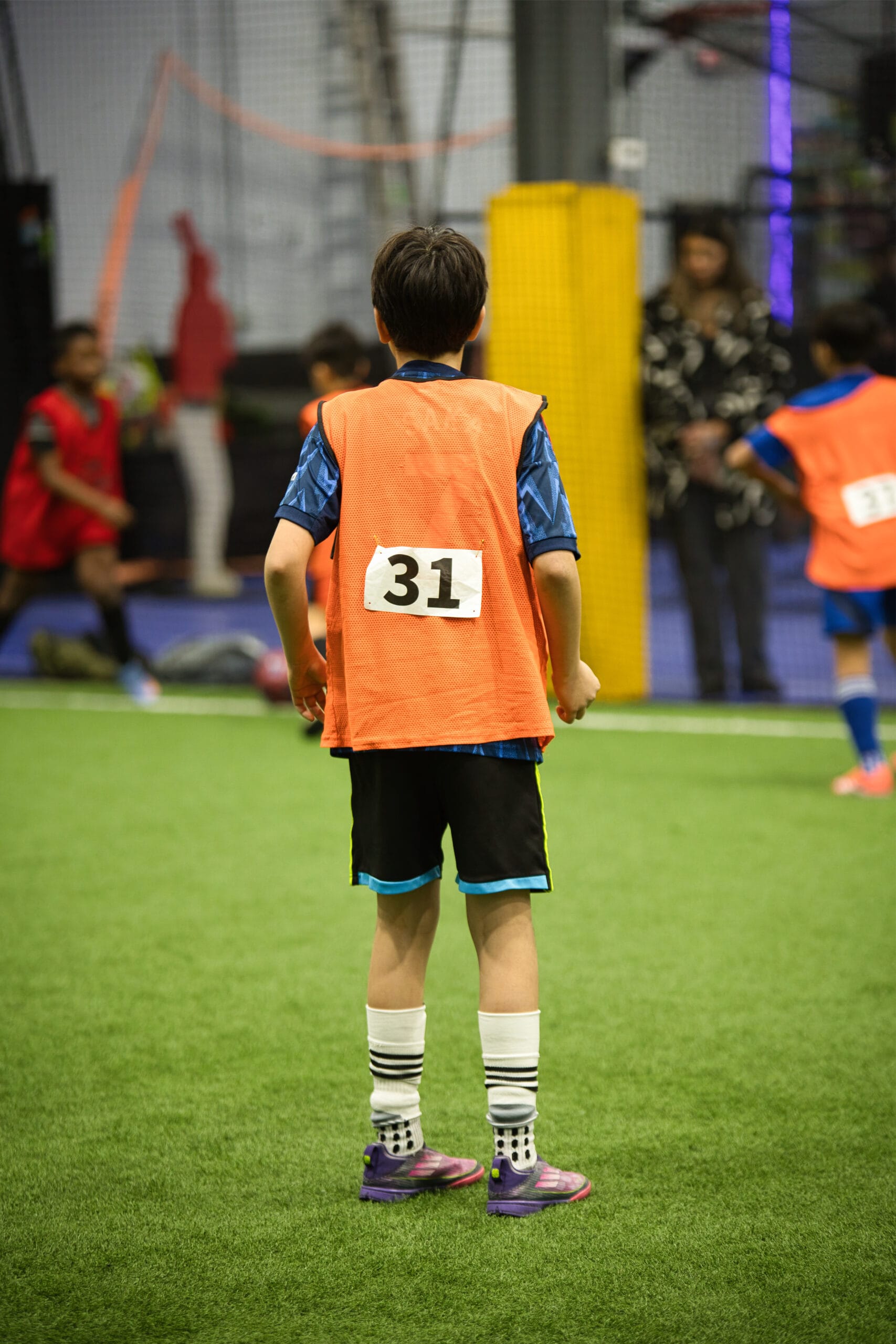 4Q8A0356 Young soccer player wearing number 31 orange pinnie standing ready during indoor tryout match.
