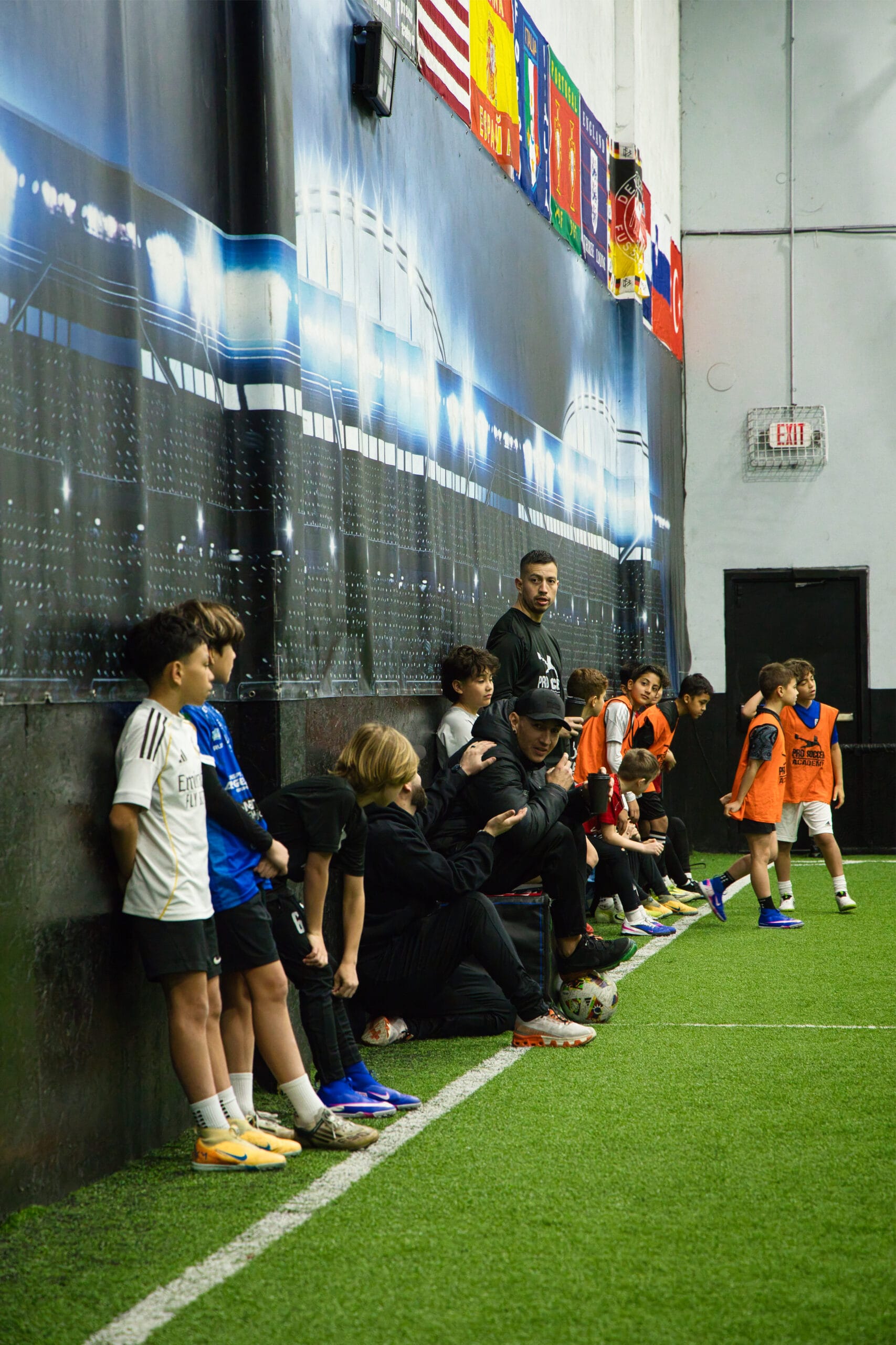 Youth soccer players sitting on sideline listening to coach during indoor training session at Pro Soccer Academy