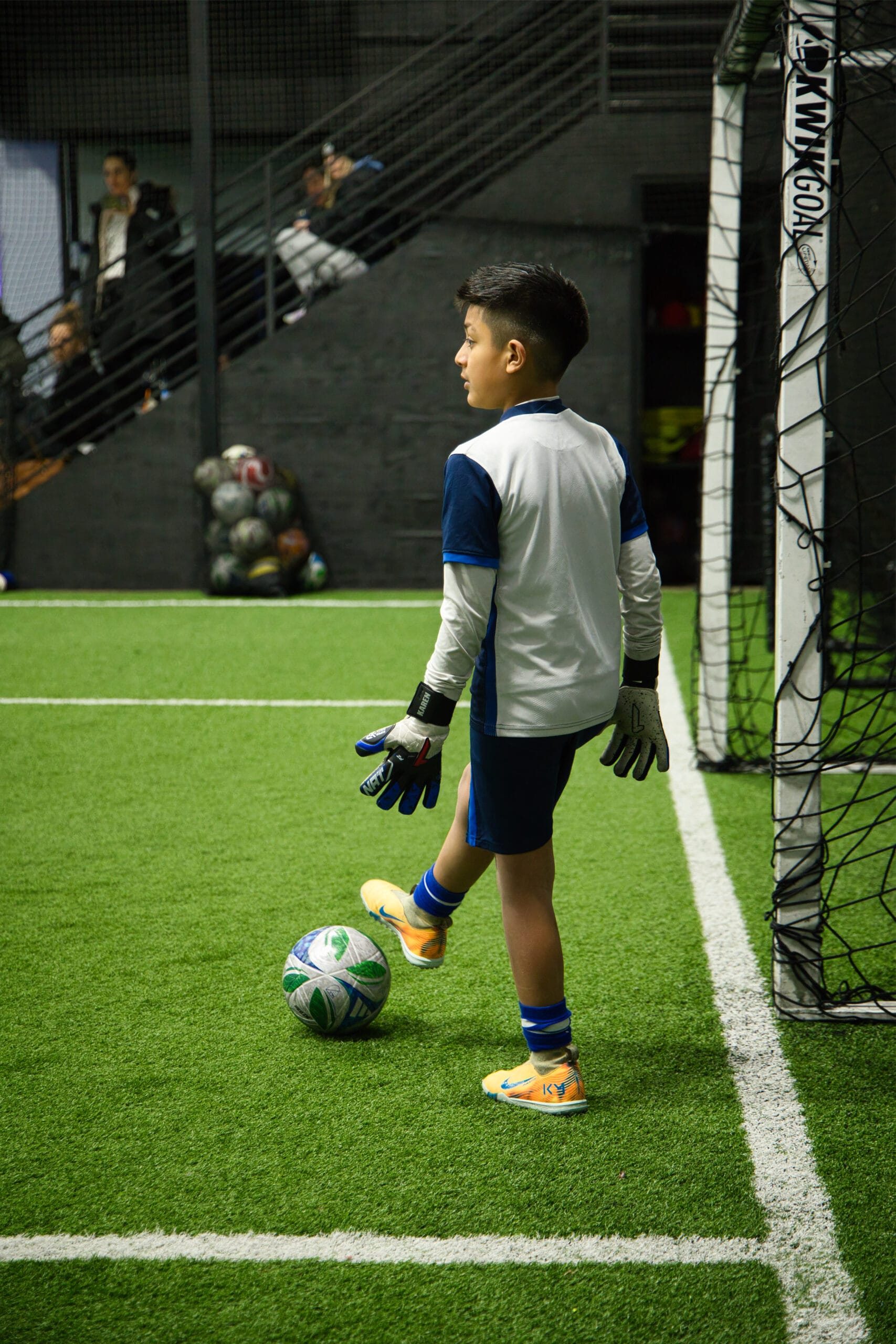 Youth goalkeeper controlling soccer ball near goal during indoor training at Pro Soccer Academy