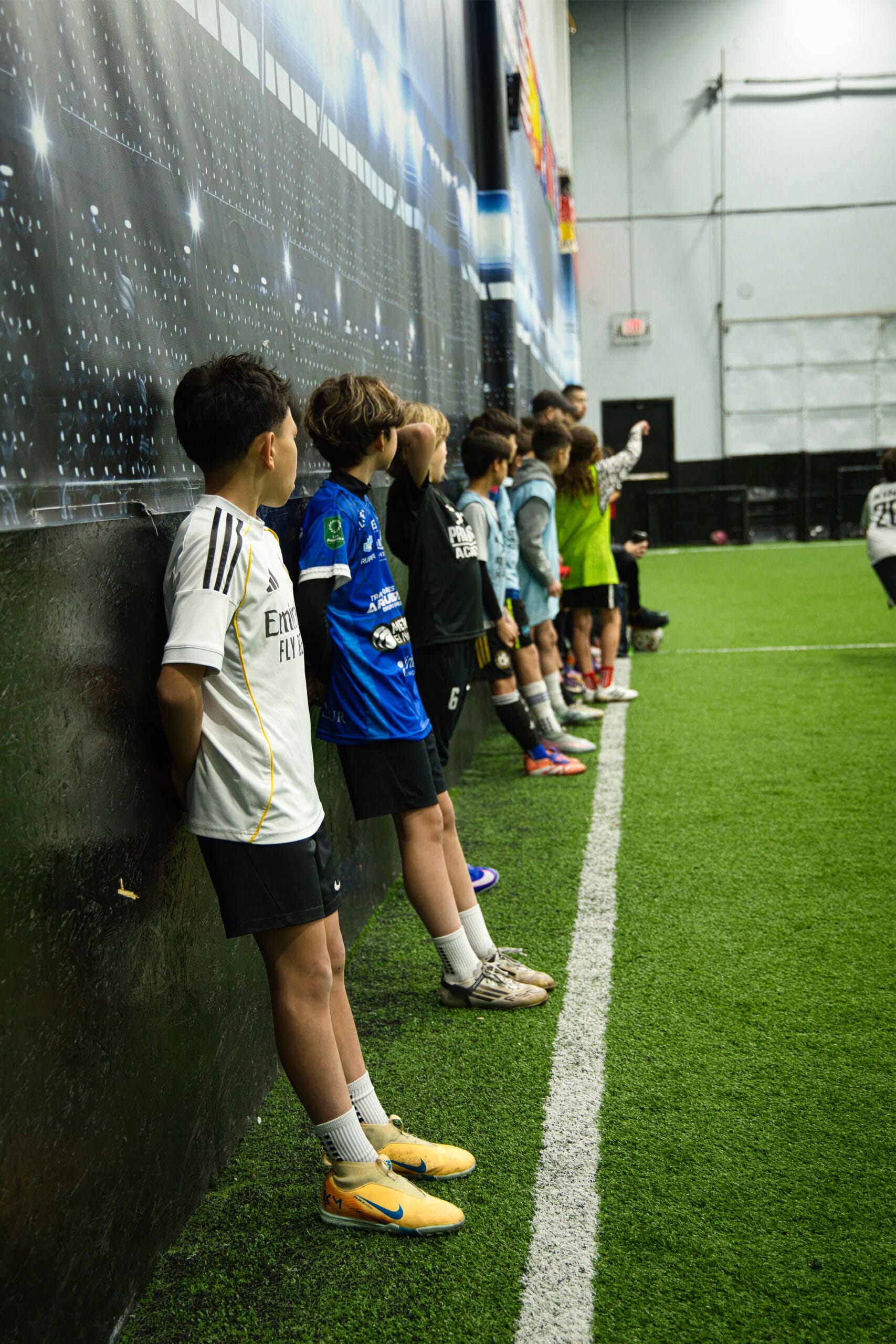 Youth soccer players lined up against wall during indoor training session at Pro Soccer Academy awaiting drill instructions