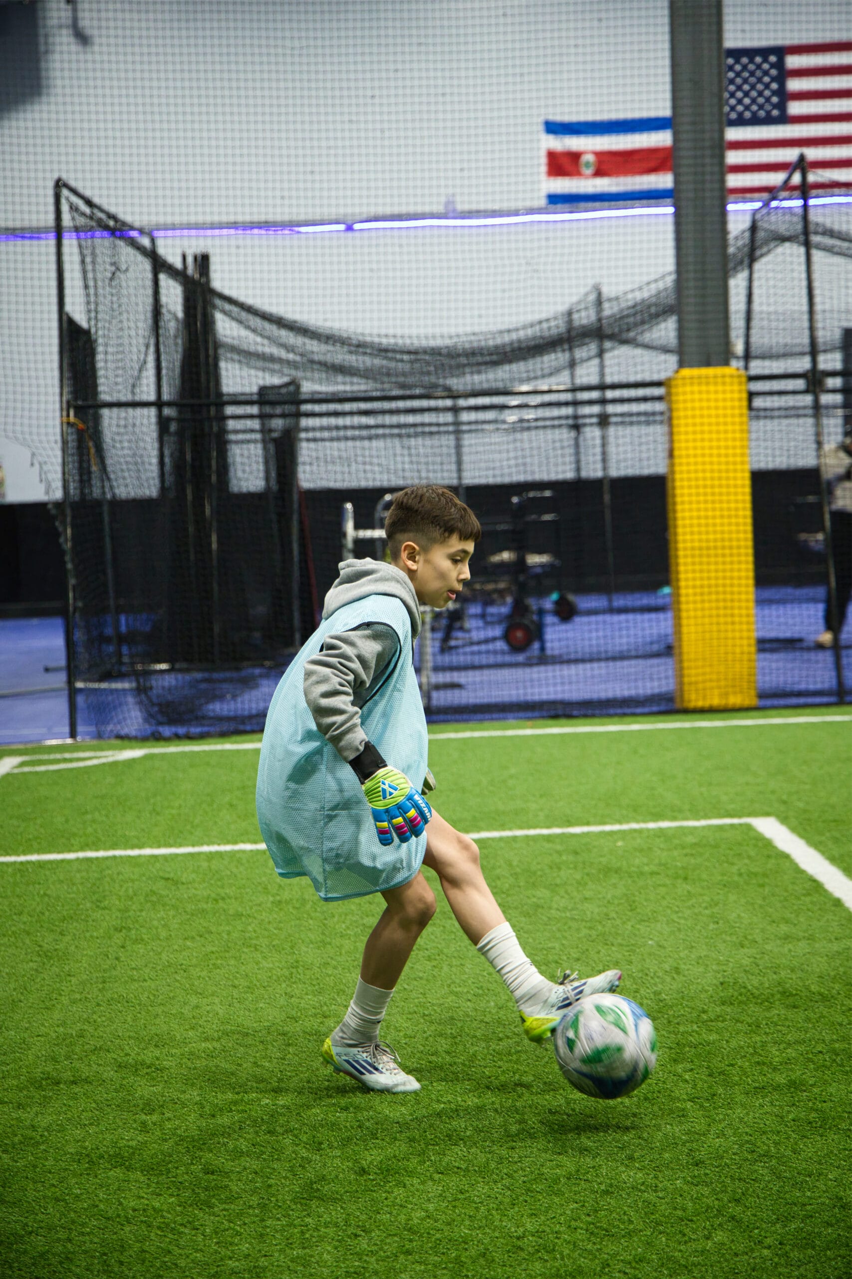 Youth goalkeeper practicing ball control during indoor soccer training session at Pro Soccer Academy facility