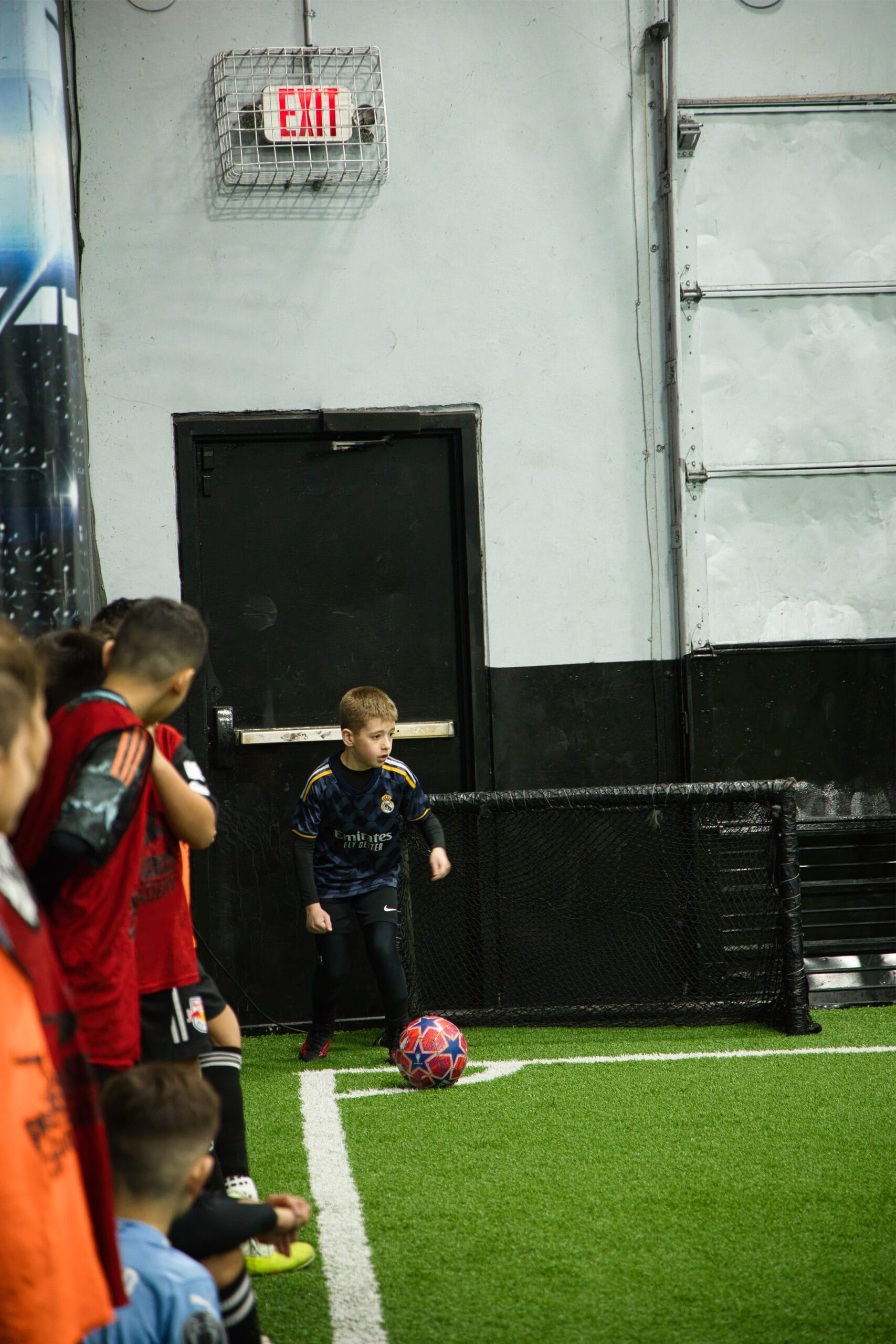 Young soccer player preparing for drill near sideline during indoor youth training session at Pro Soccer Academy