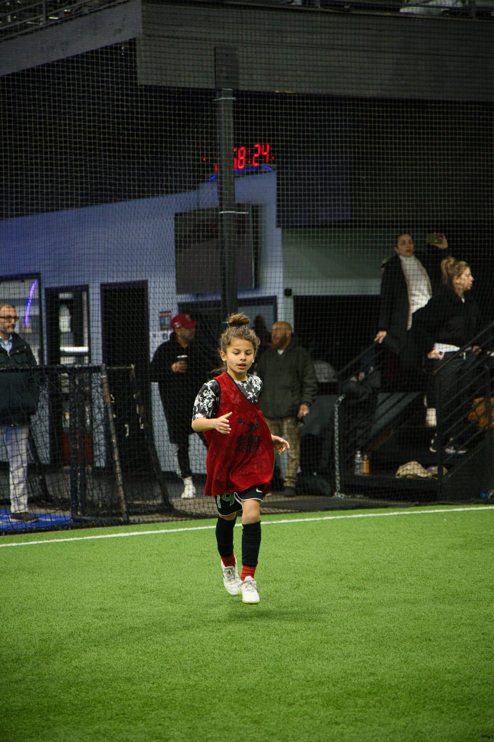 Youth soccer player running during indoor training session at Pro Soccer Academy with spectators in background